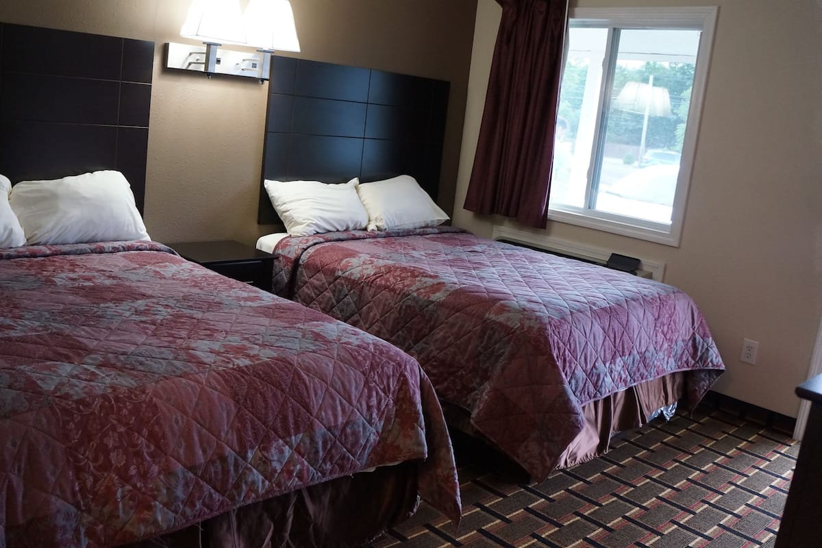 Une chambre d’hôtel avec deux lits, chacun doté d’une tête de lit, d’une fenêtre avec des rideaux et d’un luminaire fixé au mur.