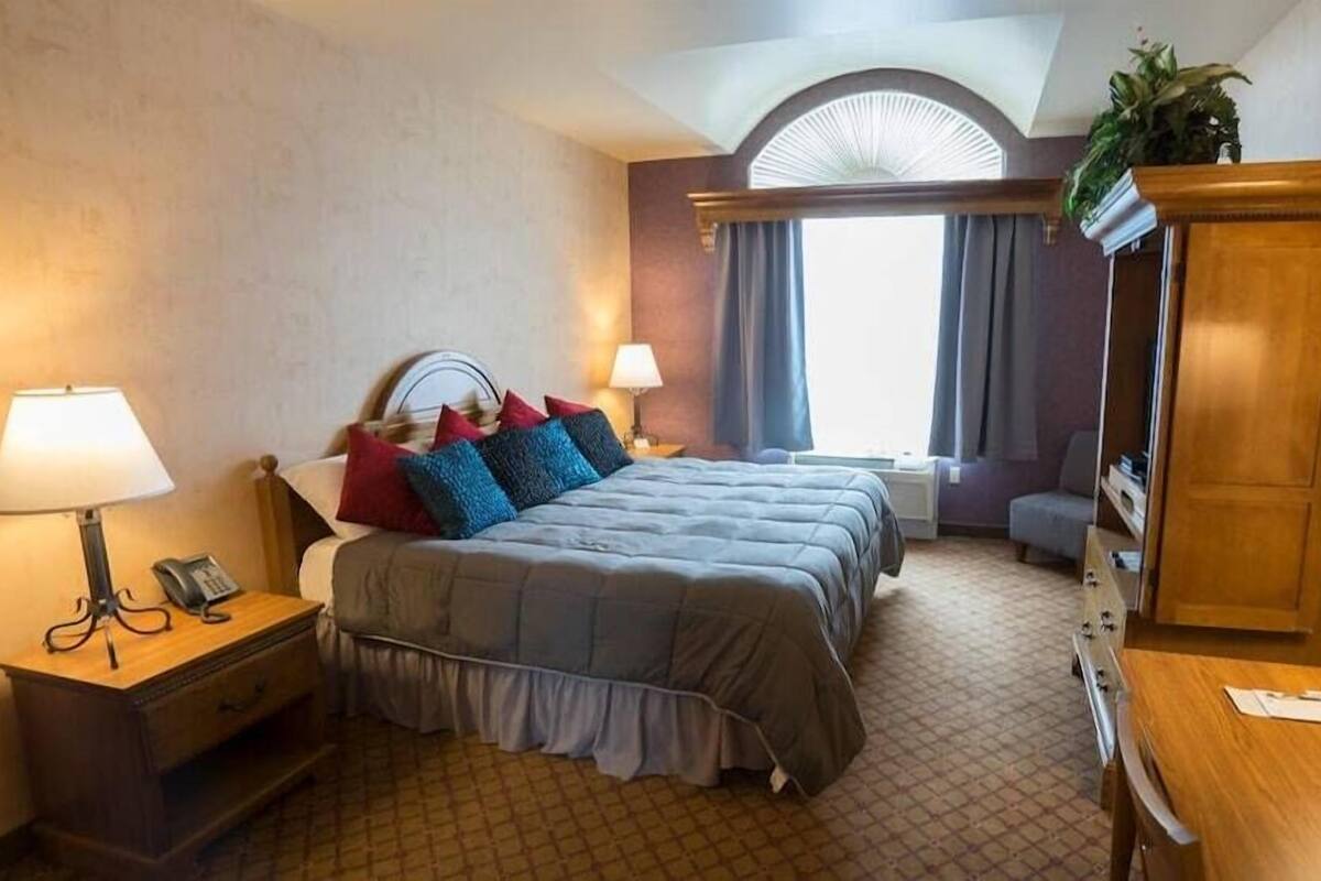 A hotel room with a bed, two bedside tables, a desk, a chair, a wardrobe, and a window with curtains.