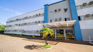 A multi-story hotel with a tiled facade, a covered entrance, and a small palm tree in the foreground. - Villalba Hoteis (Londrina)