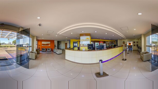 A modern hotel lobby with a reception desk, seating area, and glass doors leading outside. - Villalba Hoteis (Londrina)