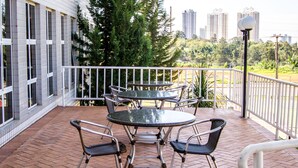 A covered outdoor patio with a round table and four chairs, surrounded by a white railing. - Villalba Hoteis (Londrina)