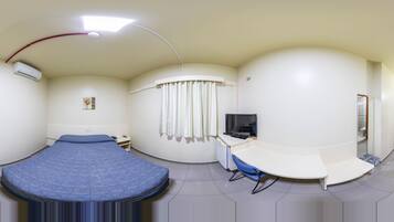 Una habitación con una cama curvada, un escritorio con una silla, un aire acondicionado, un televisor y una cortina.