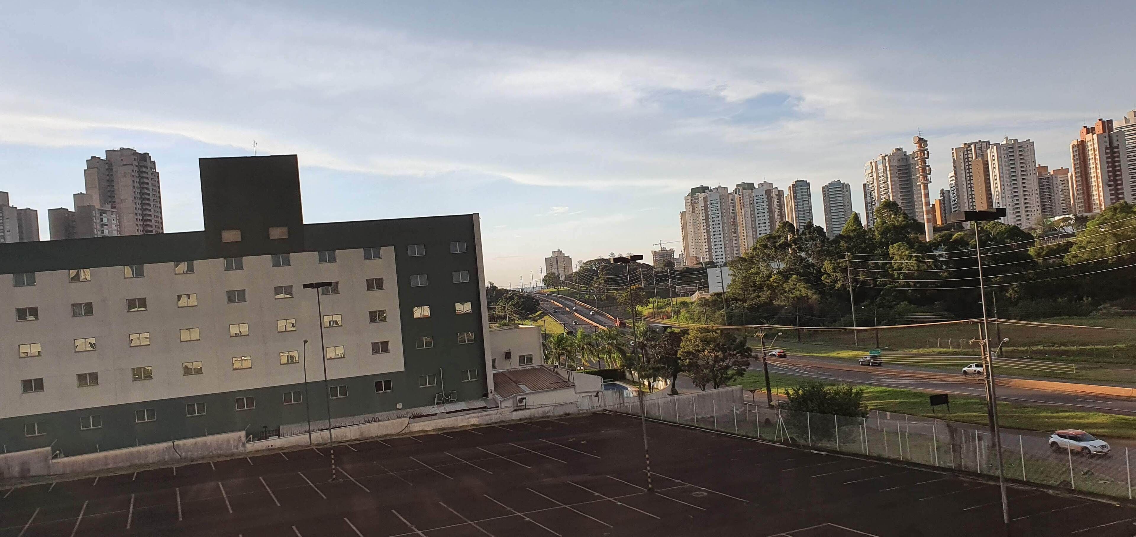 Un estacionamiento con un edificio en primer plano y rascacielos al fondo.