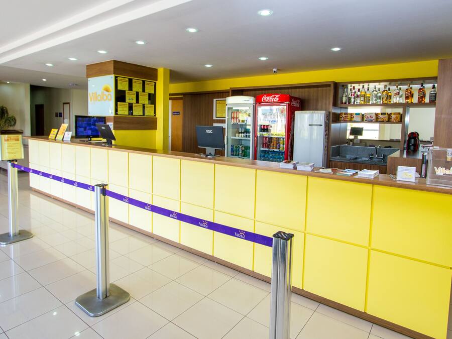 A reception area with a yellow counter, a Coca-Cola refrigerator, and a computer monitor.