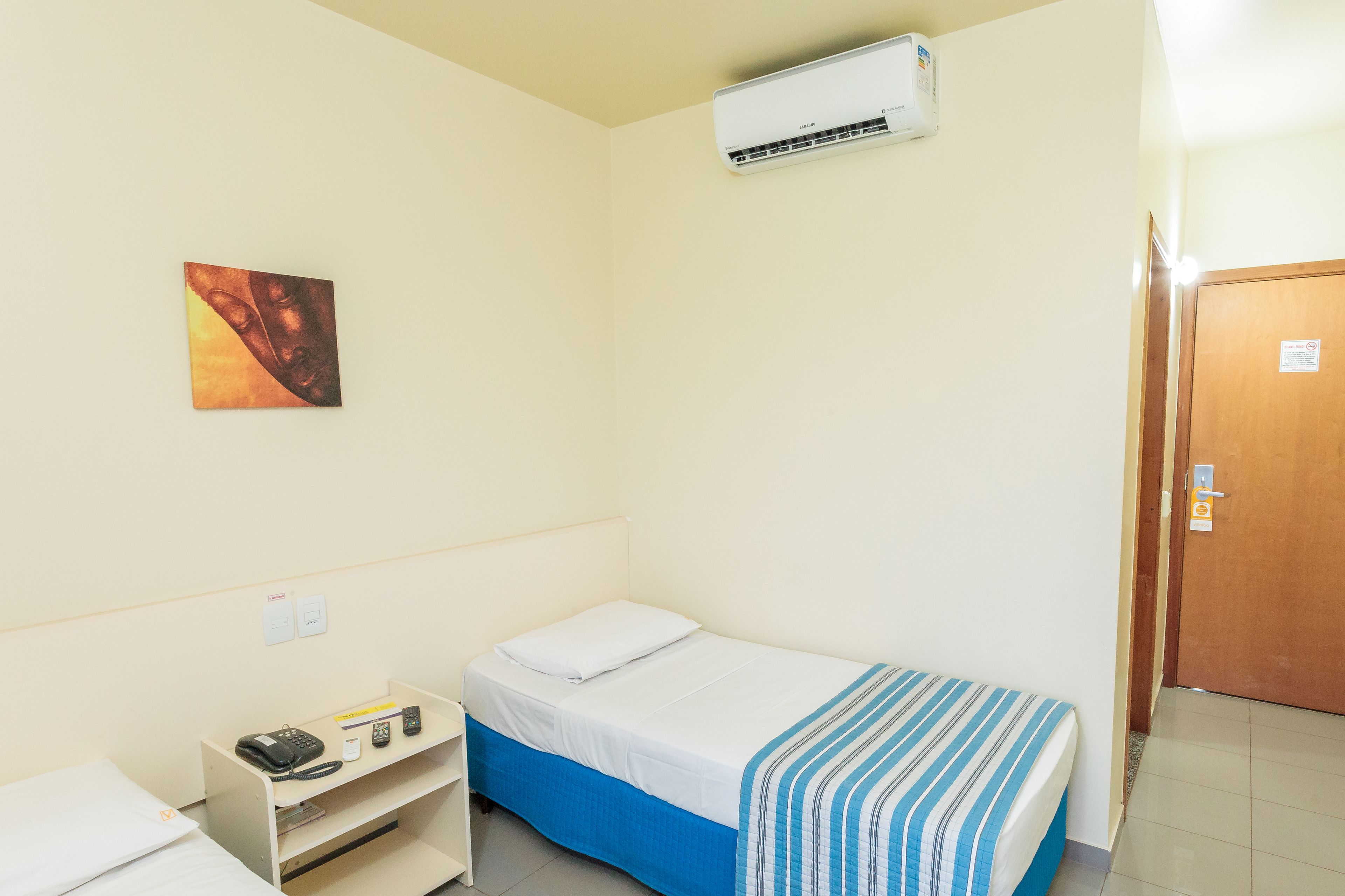 A small, single-bed room with a bed, bedside table, and an air conditioning unit.