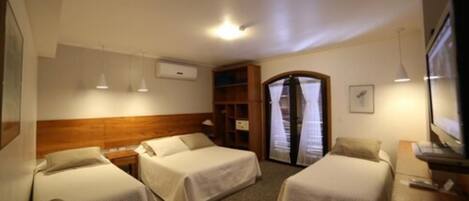 A hotel room with two single beds, a wooden headboard, a desk with a computer, a TV, and a bookshelf.