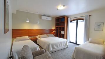 Ein Hotelzimmer mit zwei Betten, einem Sofa, einem Holzkopfteil, einer Deckenleuchte, einer Klimaanlage, einem Fenster mit Vorhängen und einem gerahmten Bild an der Wand.