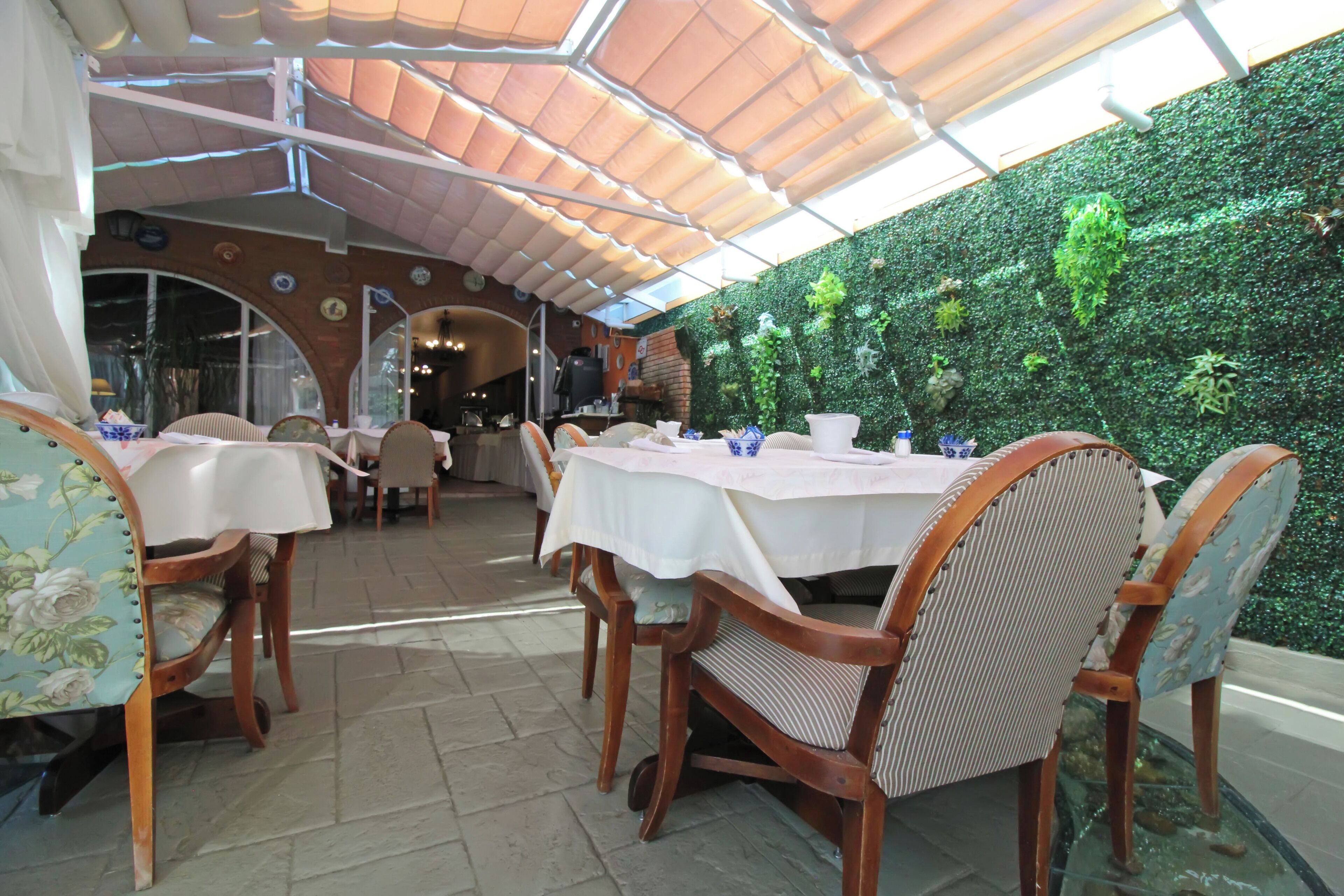 An indoor dining area with tables and chairs, a green wall with plants, and a tiled floor.