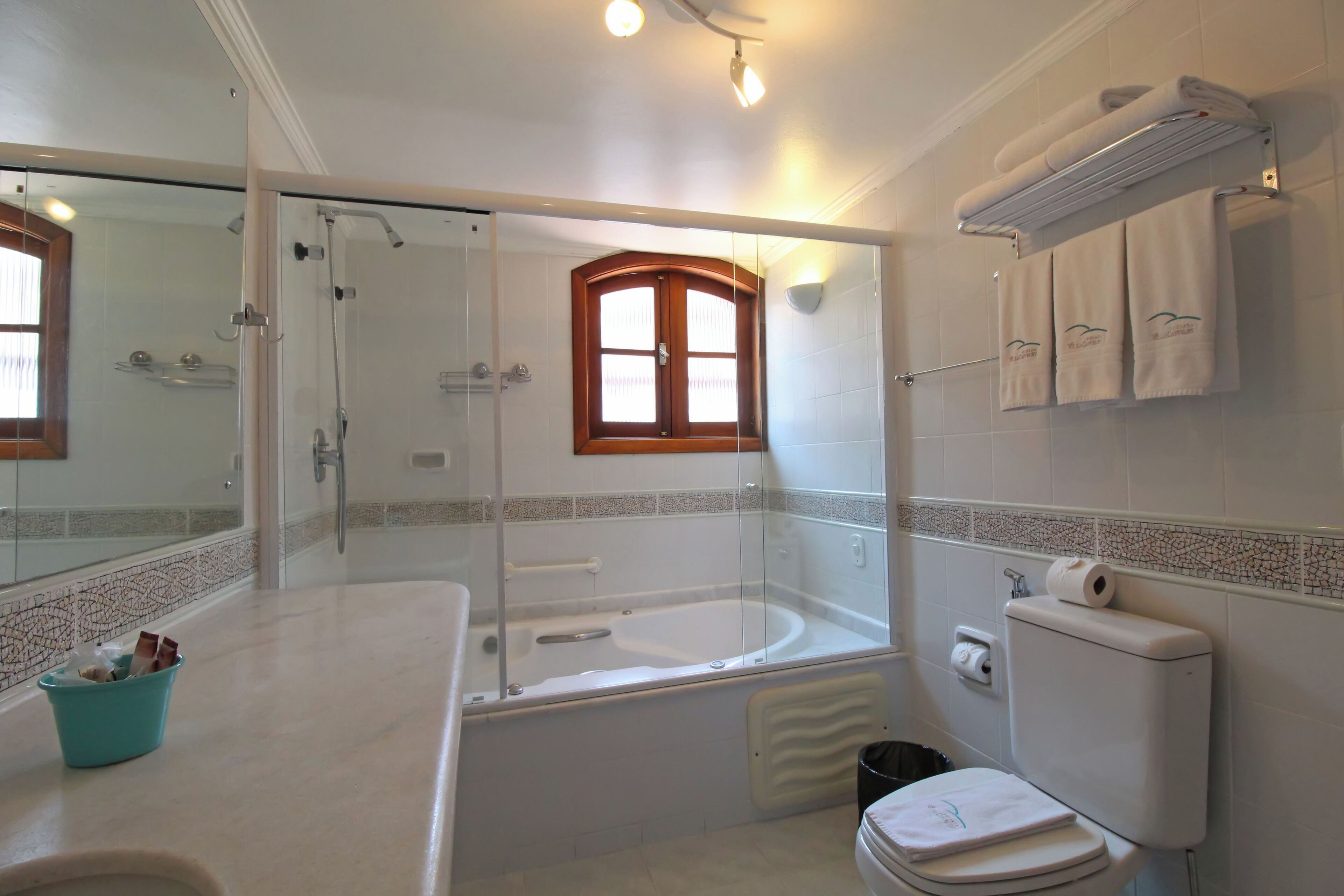 A bathroom with a glass-enclosed shower, a bathtub, a toilet, and a sink with a mirror.