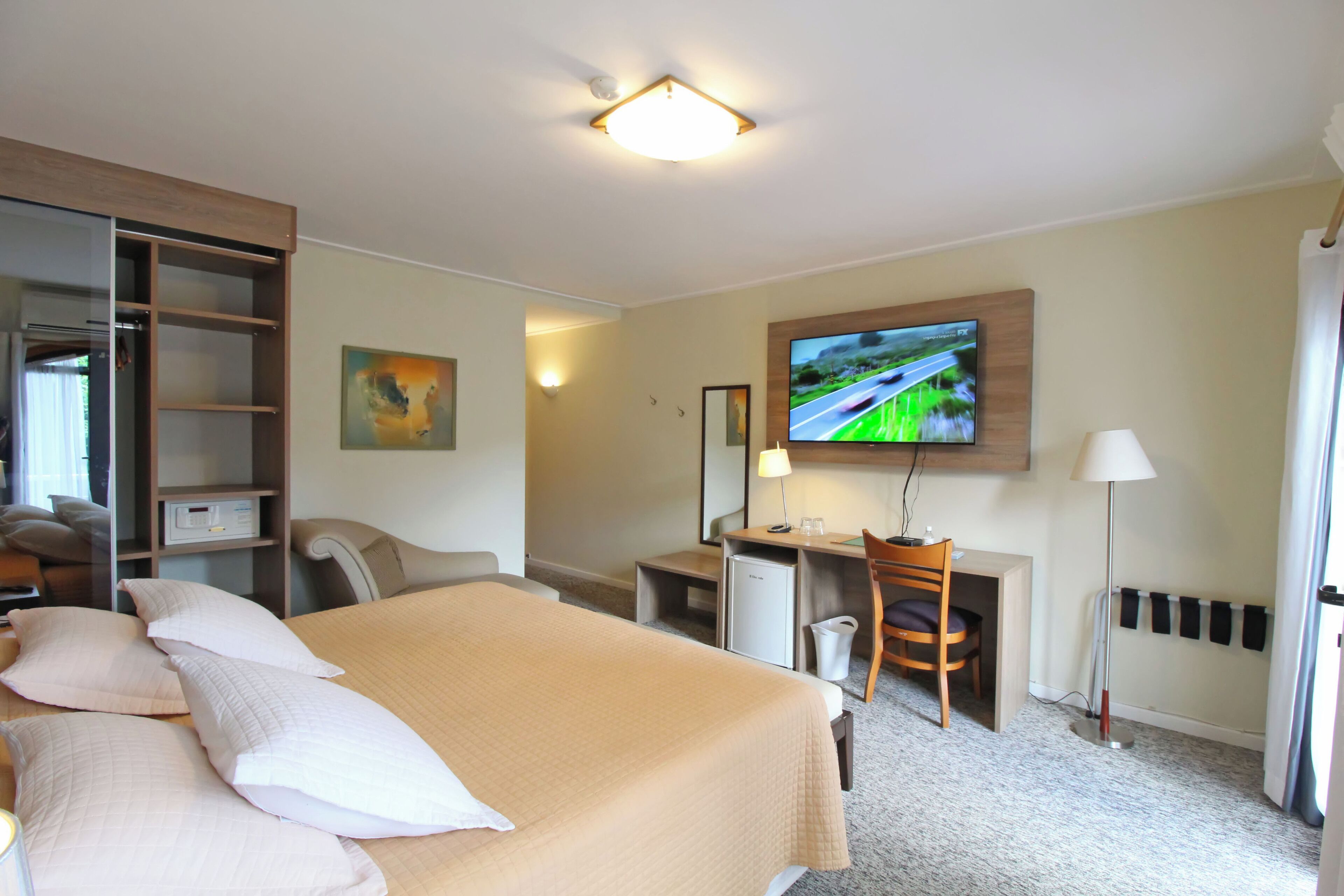 Una habitación de hotel con cama, escritorio, silla, televisor y armario.