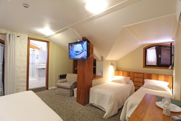 A hotel room with two beds, a TV mounted on a wooden pillar, a small table with a bottle and remote, and a bathroom visible through an open door.
