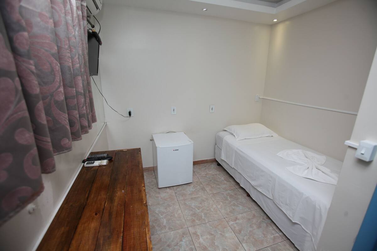 A small, clean room with a bed, a small table, and a refrigerator.