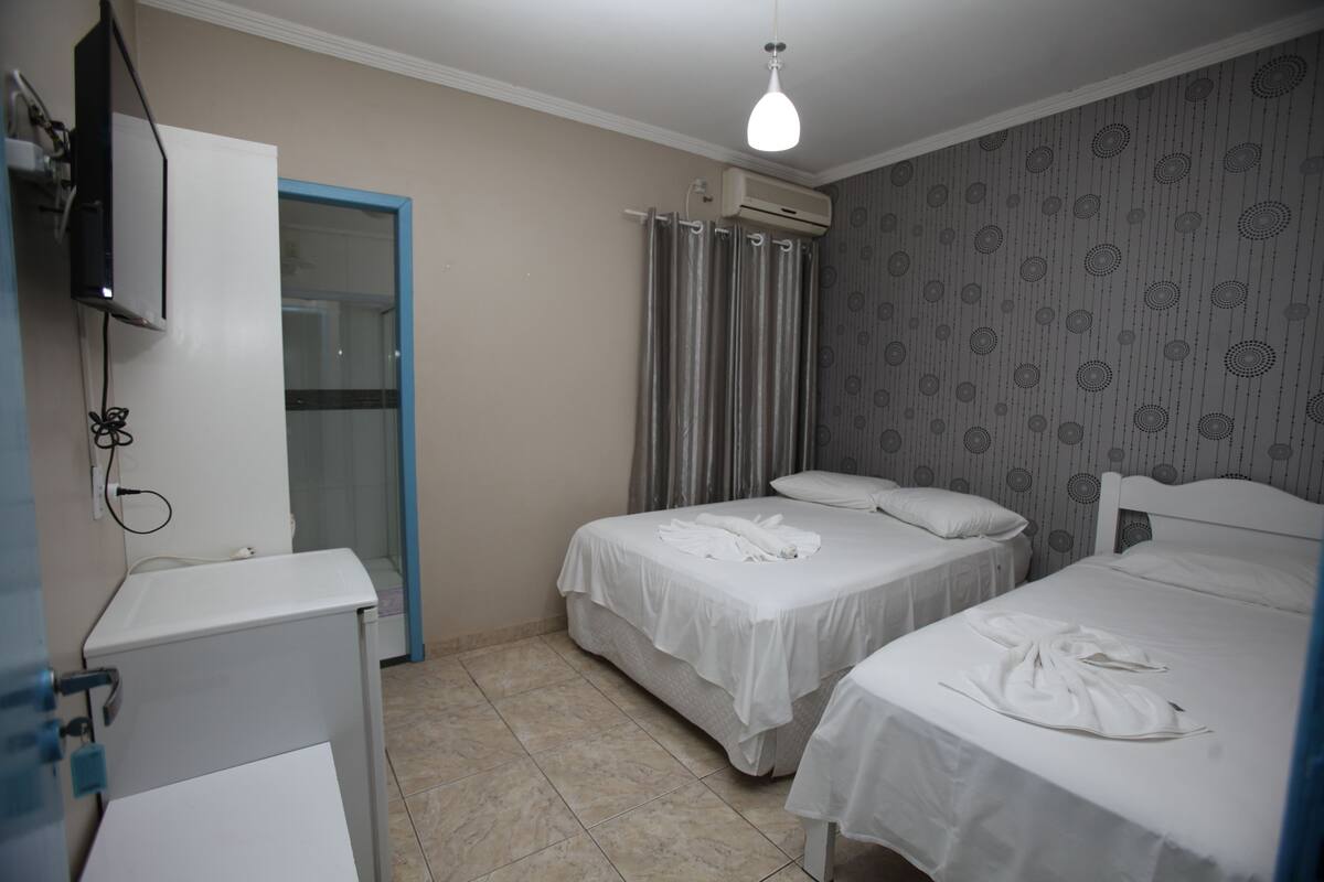 A hotel room with two beds, a wardrobe, an air conditioning unit, and a shower area.