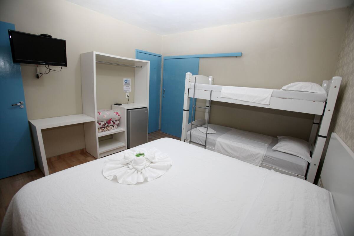 A hotel room with a bunk bed, a desk, a wardrobe, and a flat-screen TV.