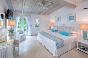 A spacious bedroom with a large bed, a sitting area with a chair, a television, and a desk with a lamp. - Condos on Glitter Bay Estate by Blue Sky Luxury (Holetown)
