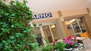 Fachada con un letrero que dice "ARNO" y una exhibición de plantas y flores.