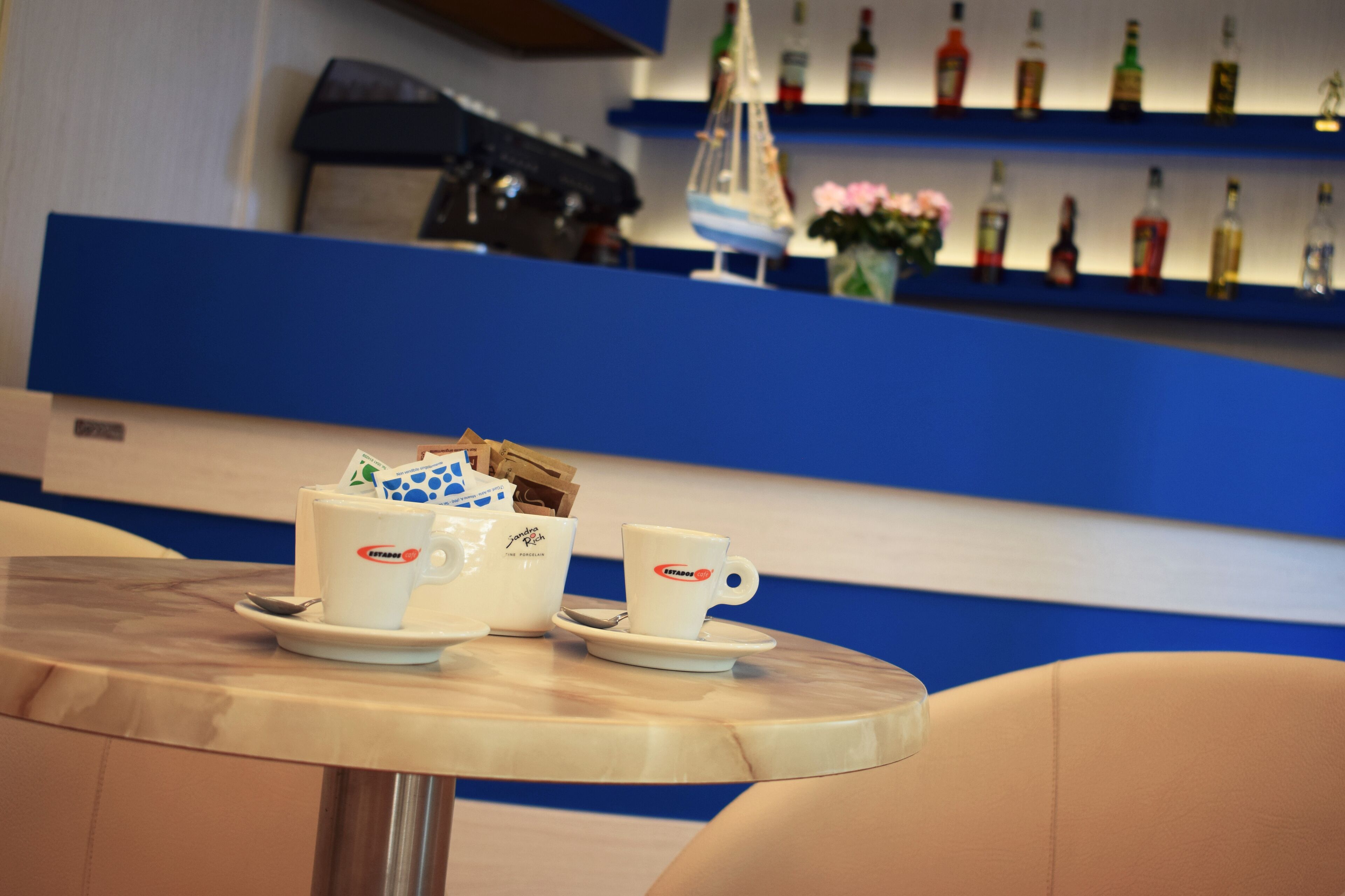 A bar area with two white cups on a table, a ship model, and a row of liquor bottles on shelves.
