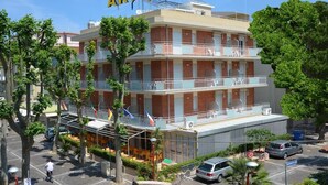 Un hotel de varios pisos con balcones, una zona de estar exterior cubierta y un estacionamiento.