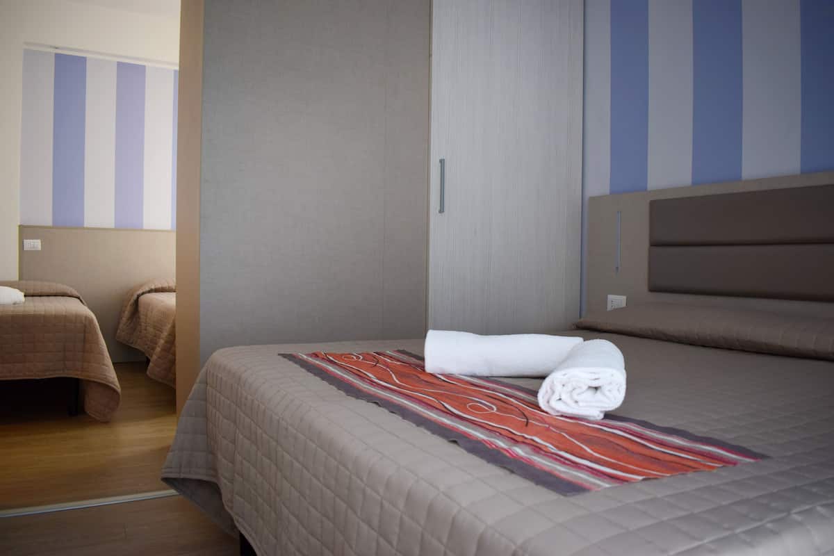 A hotel room with a large bed, two smaller beds, and a striped wall.