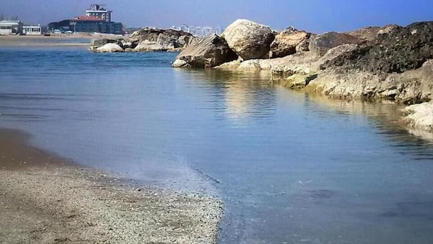 Paisaje costero con agua cristalina, costa rocosa y un edificio distante.