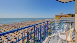 A balcony with a view of a beach, blue railings, and white plastic chairs. - Hotel Napoleon (Jesolo)