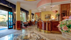 A hotel lobby with a reception desk, seating area, and a large window. - Hotel Napoleon (Jesolo)