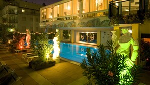 A hotel with a swimming pool, outdoor seating, and decorative statues. - Hotel Napoleon (Jesolo)