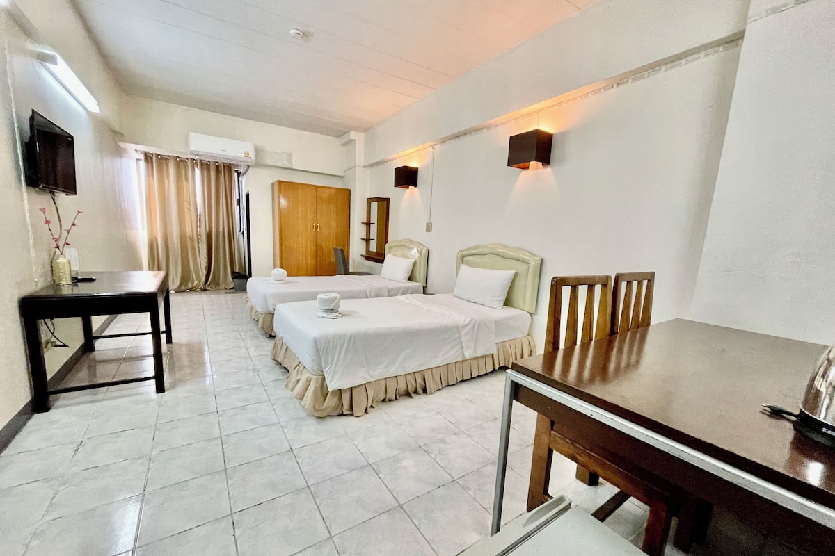 A hotel room with two single beds, a wooden table, a TV, and a desk with a vase.