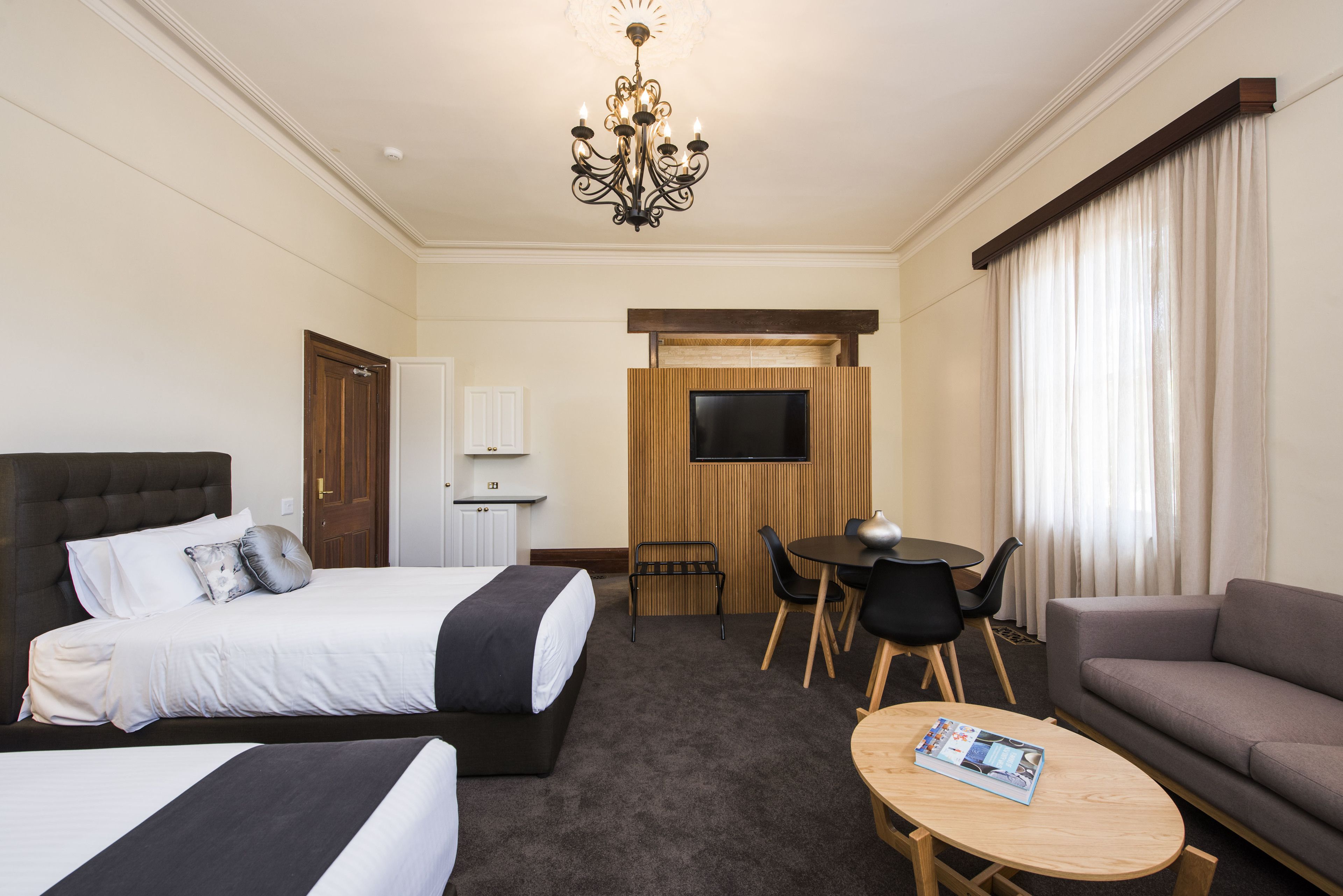 Una habitación de hotel con una cama grande, un sofá, una mesita, un televisor y una araña.