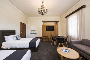Una habitación de hotel con una cama grande, un sofá, una mesita, un televisor y una araña.