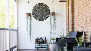 Un porche techado con suelo de madera, muebles de mimbre, plantas colgantes y una pared de ladrillo.