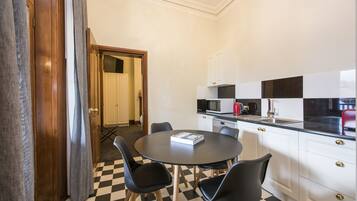 Cocina compacta con piso a cuadros, una mesa redonda con sillas y armarios blancos con detalles dorados.