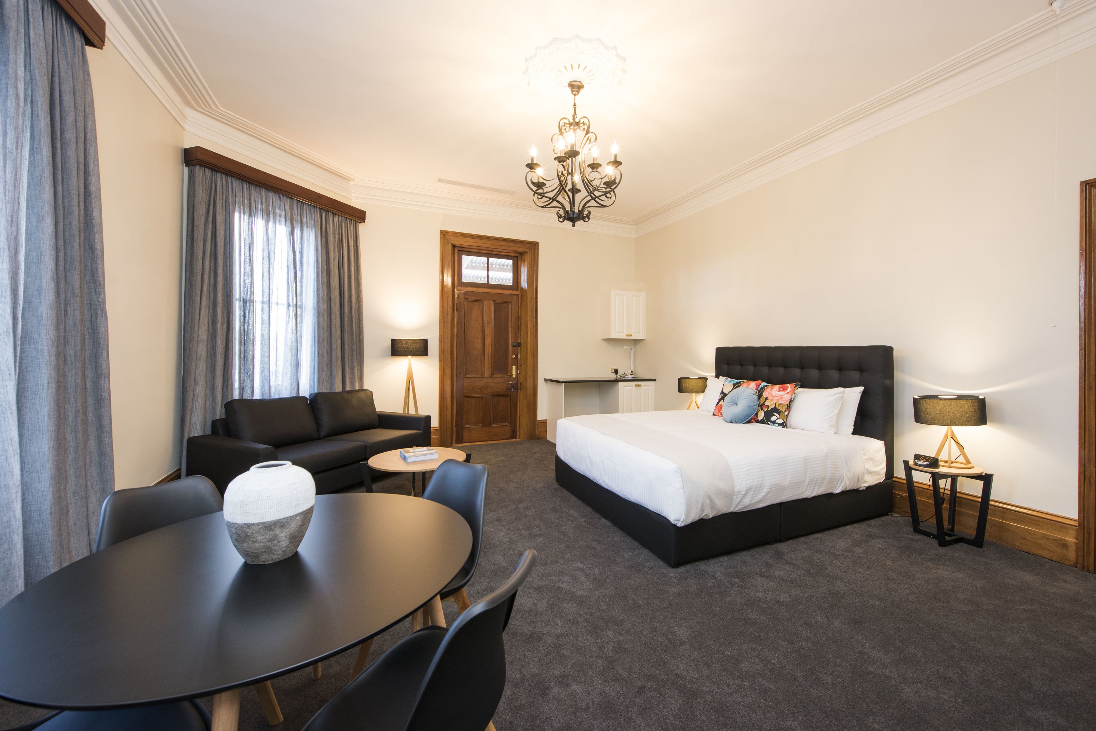 A hotel room with a bed, a sofa, a dining table, and a chandelier.