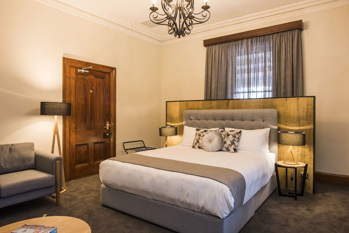 A hotel room with a large bed, a sofa, a desk, and a chandelier.