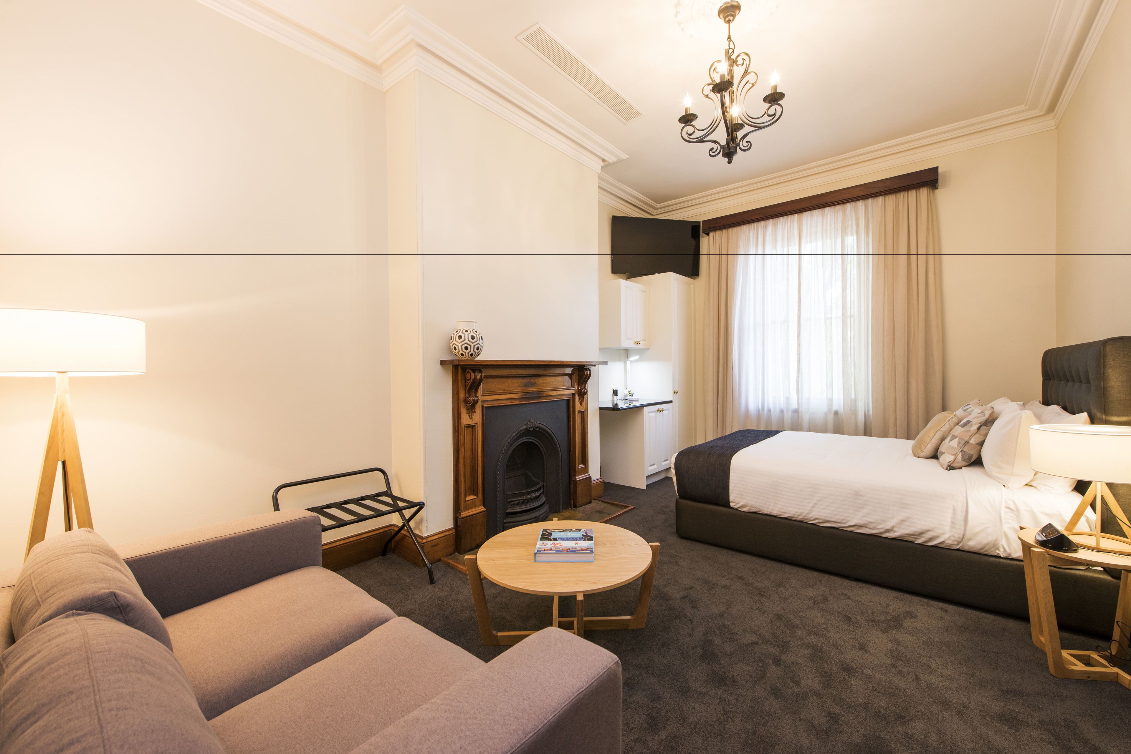 A hotel room with a sofa, a bed, a fireplace, a TV mounted on the wall, and a window with curtains.
