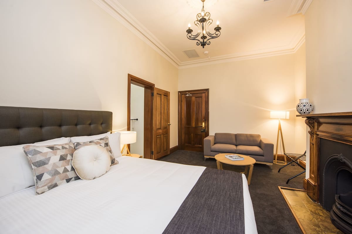 A hotel room with a large bed, a sofa, a small table, a fireplace, and a chandelier.