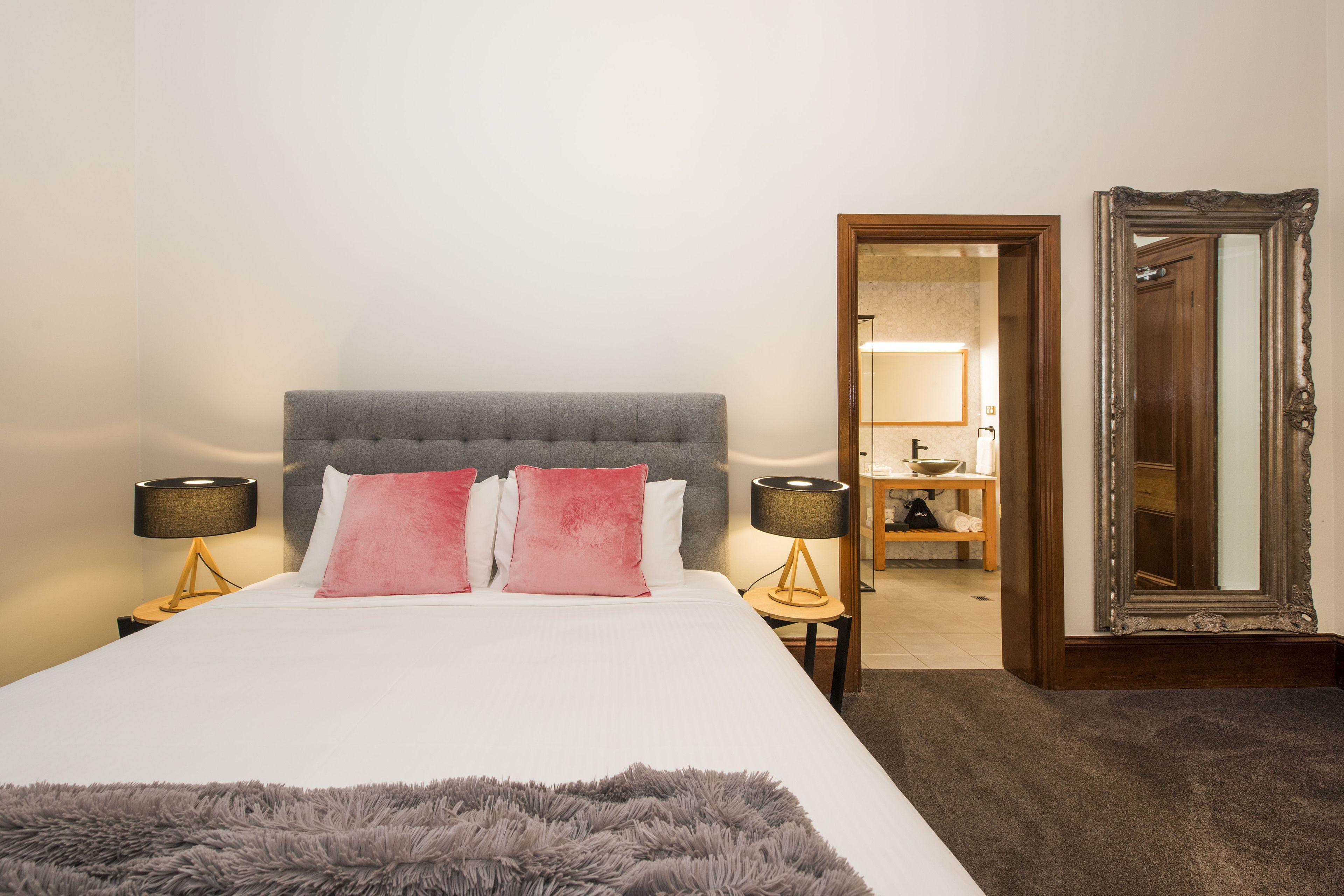 Una cama bien hecha con cabecera gris, dos lámparas de noche y un suave plaid gris.