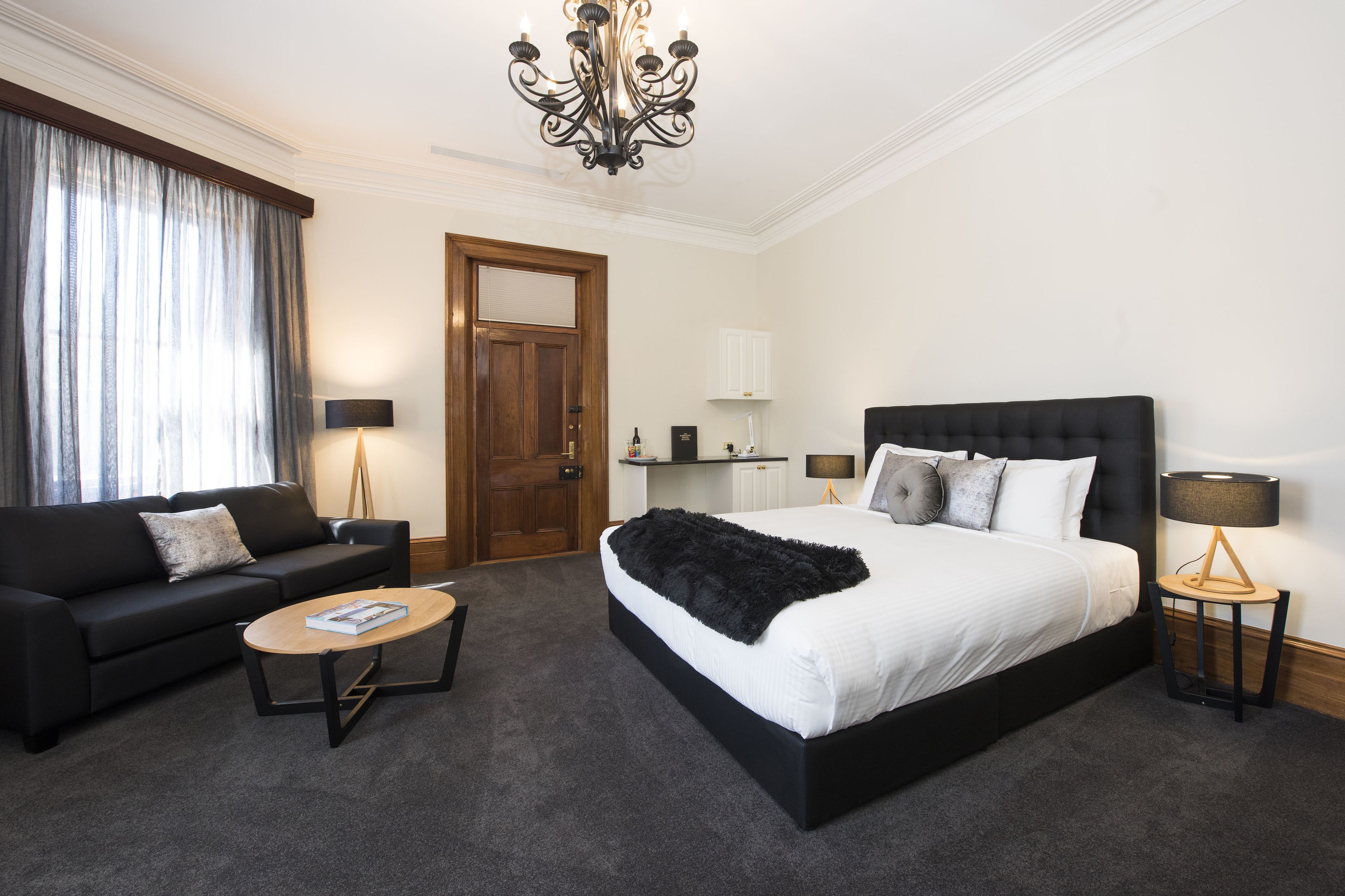 A hotel room with a large bed, a sofa, a coffee table, a chandelier, and a door.