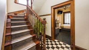 Una escalera con barandillas de madera y escalones alfombrados que conduce a un dormitorio con piso a cuadros y una cama.