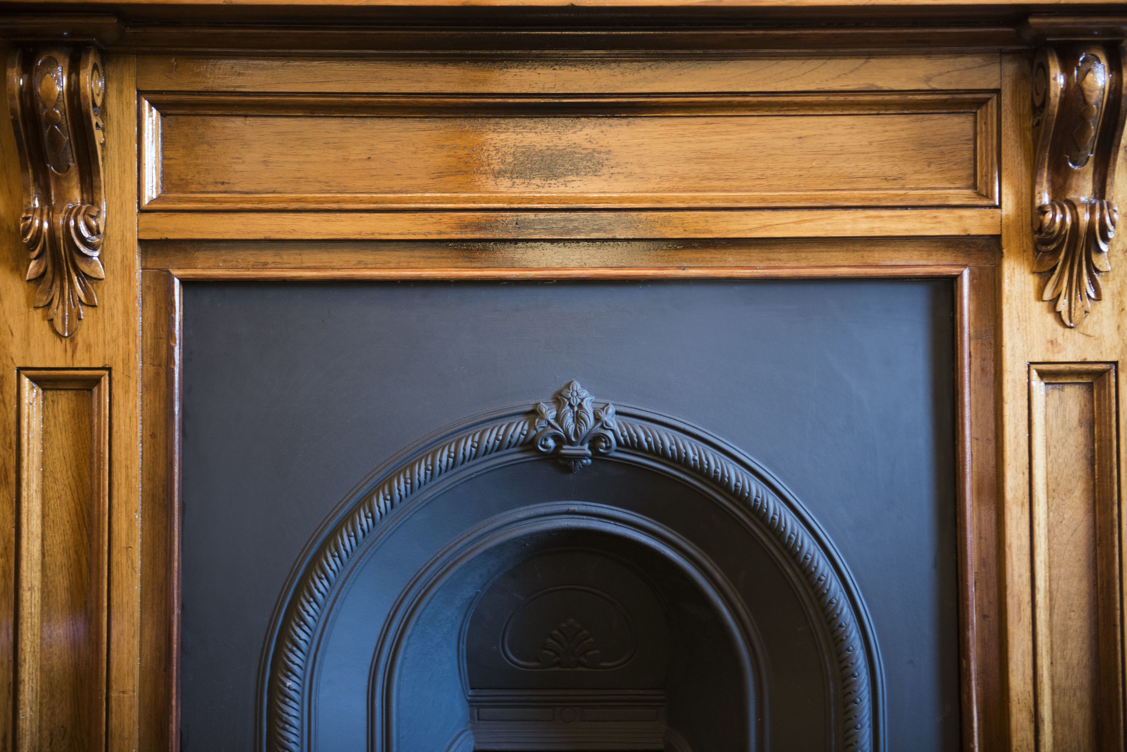 Een houten openhaard met gedetailleerde houtsnijwerken en een donkere omlijsting.