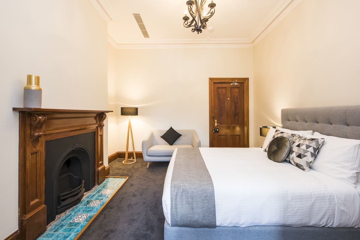 A hotel room with a fireplace, a bed with grey bedding, a grey upholstered sofa, and a wooden door.
