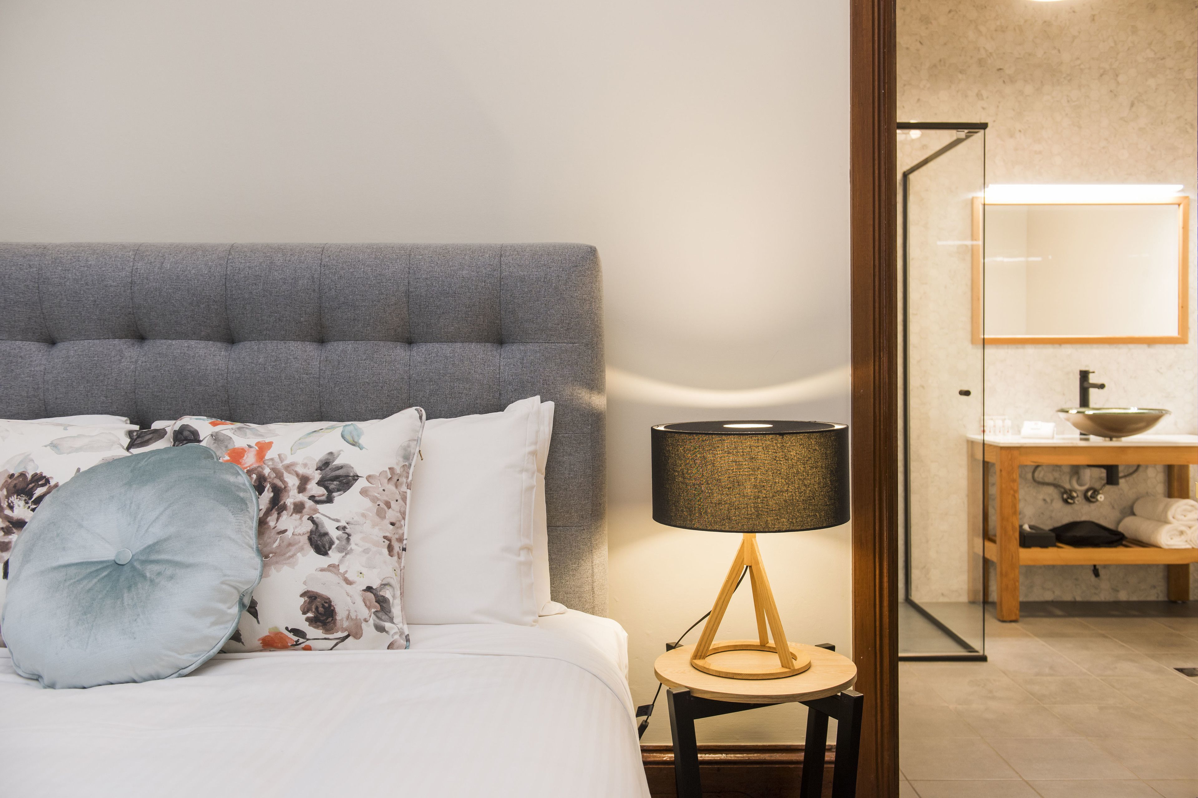 A neatly made bed with a grey headboard, a bedside lamp, and a floral pillow.