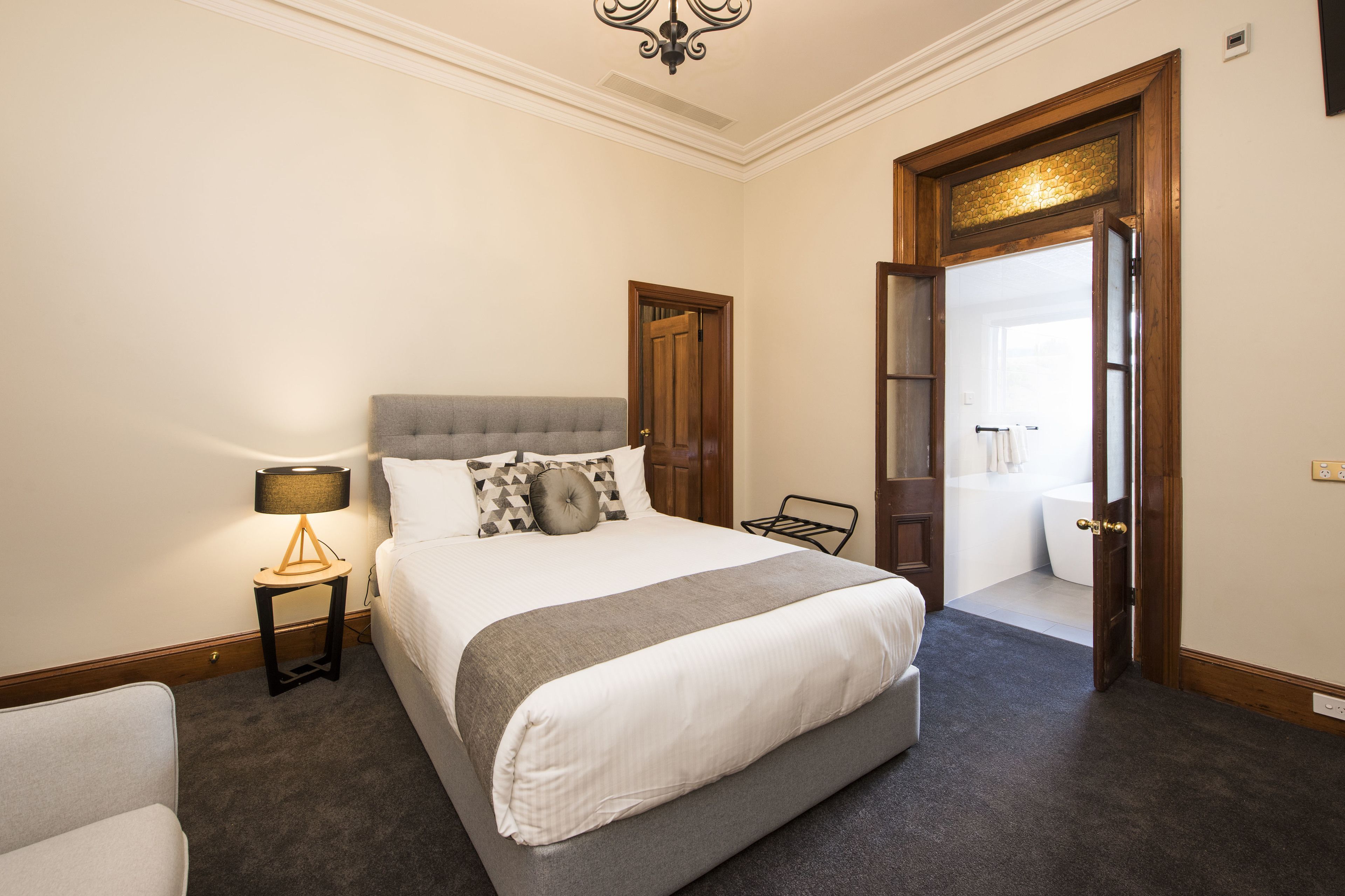 Une chambre à coucher bien aménagée, avec un grand lit, une table de chevet avec une lampe et une porte donnant sur une salle de bain.