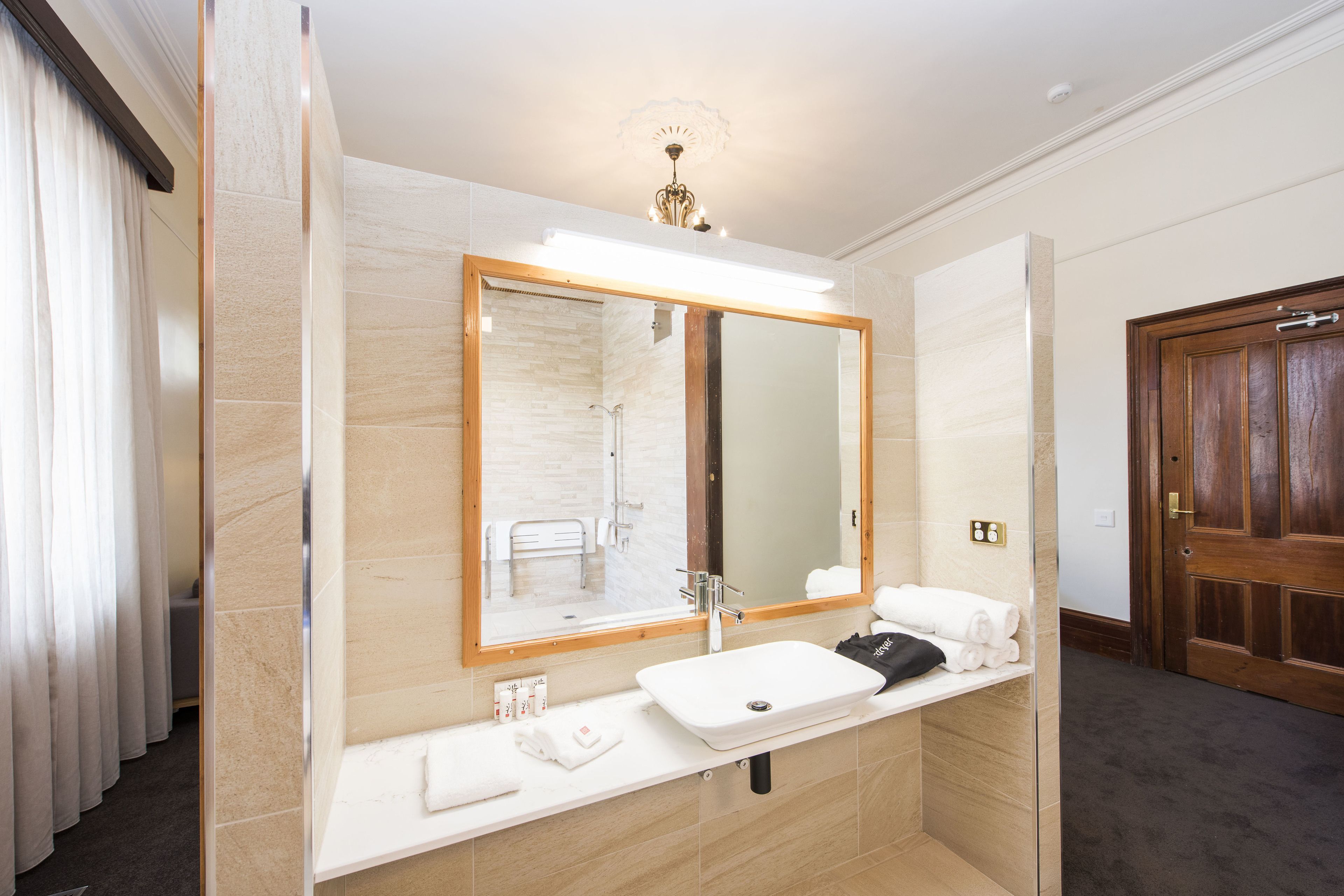 A modern bathroom with a large mirror, white sink, and a shower area.