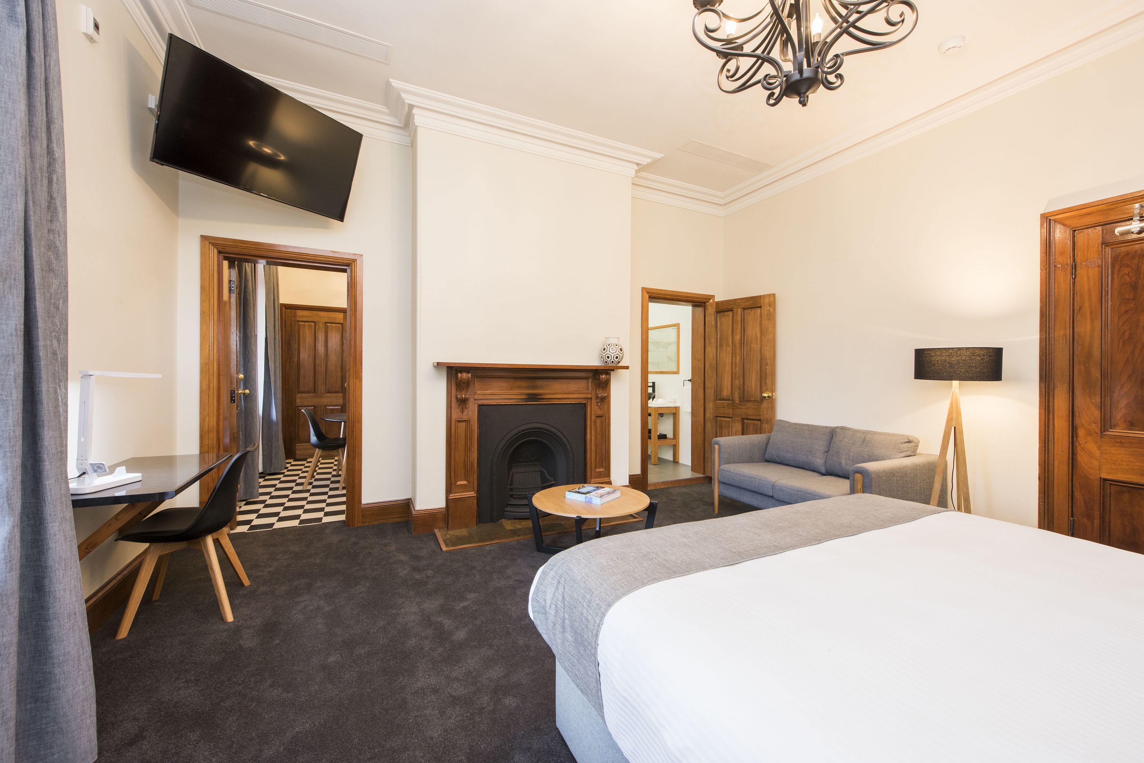 A hotel room with a bed, a sofa, a small table, a fireplace, a television, and a door leading to another room.