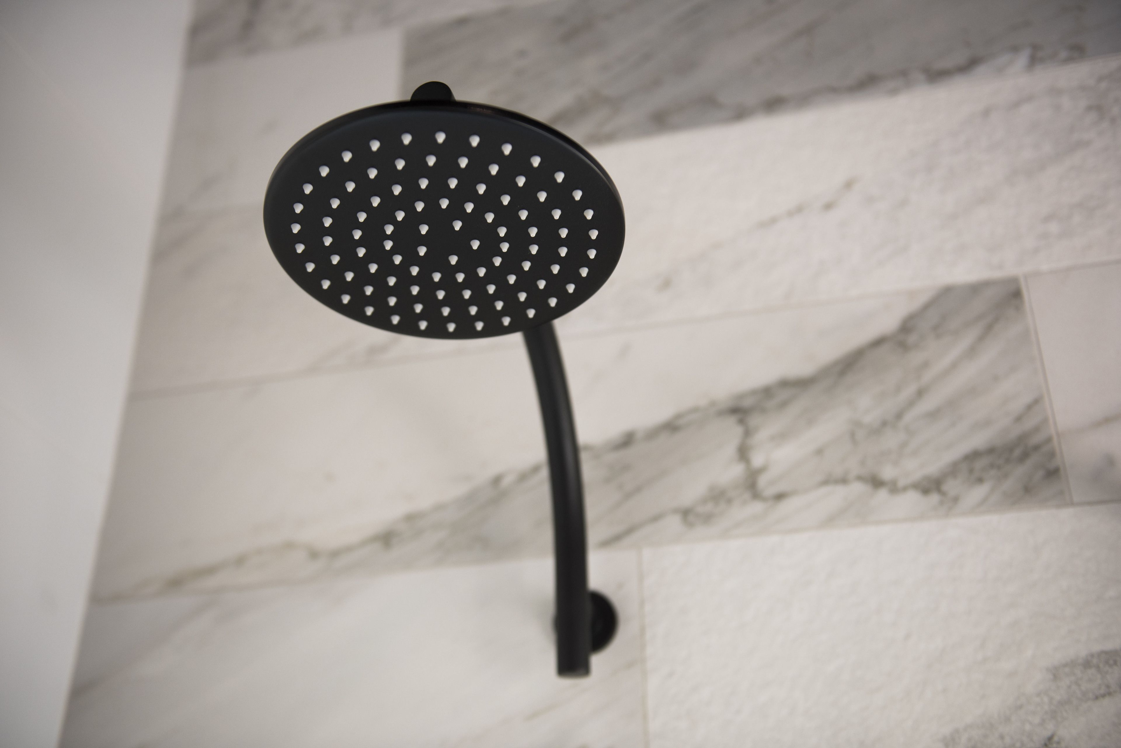 A black showerhead mounted on a wall with a marble tile pattern.