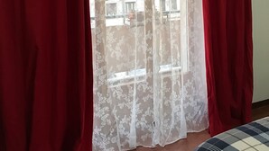Une chambre avec un lit, des rideaux rouges et une fenêtre donnant sur des immeubles.