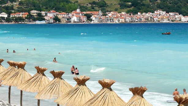 A beach with straw umbrellas and a view of a coastal town.