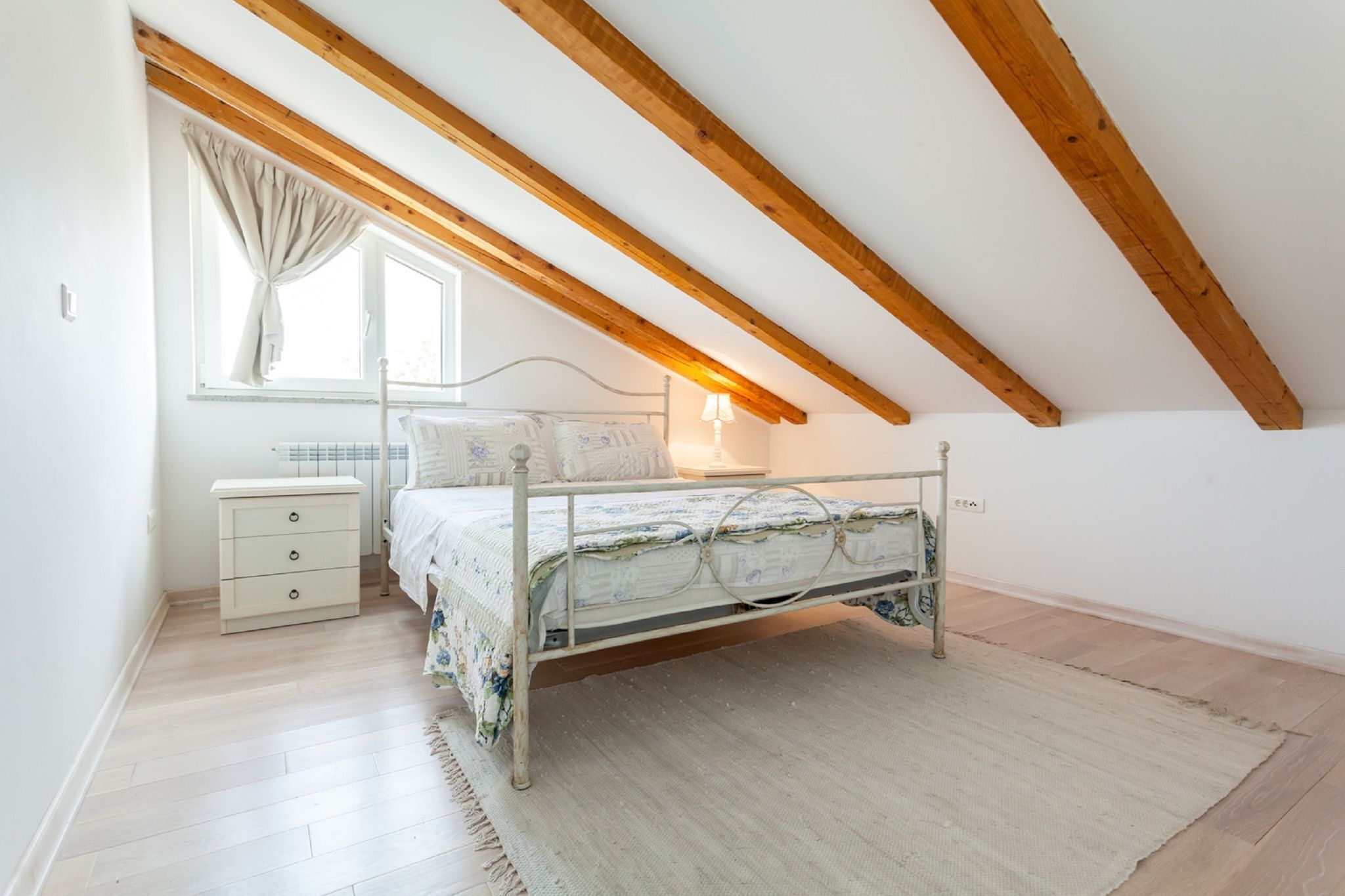 Una camera da letto con soffitto spiovente, un letto con struttura in metallo, un comodino e una lampada.