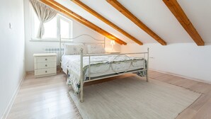 A bedroom with a sloped ceiling, a bed with a metal frame, a bedside table, a nightstand, a window with curtains, and a light fixture.
